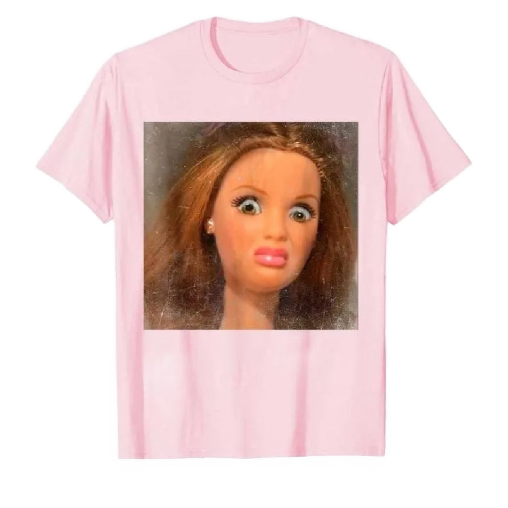 Pink t-shirt with a printed design of a doll's face on a white background